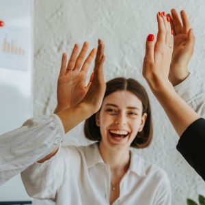 Diverse colleagues share a joyful high five, showcasing teamwork and unity in the office.